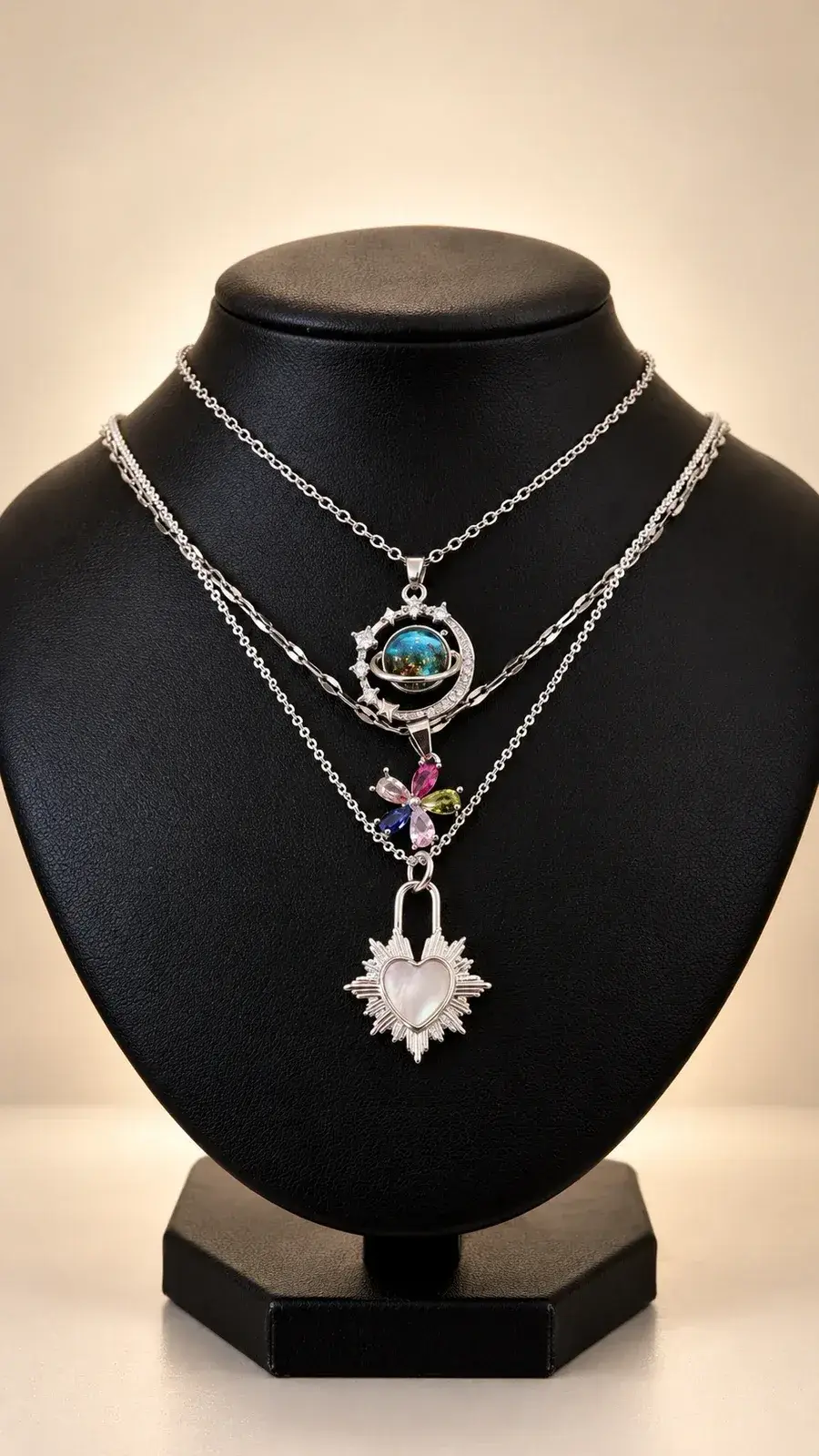 Tres collares plateados con dijes: planeta, flor de colores y corazón