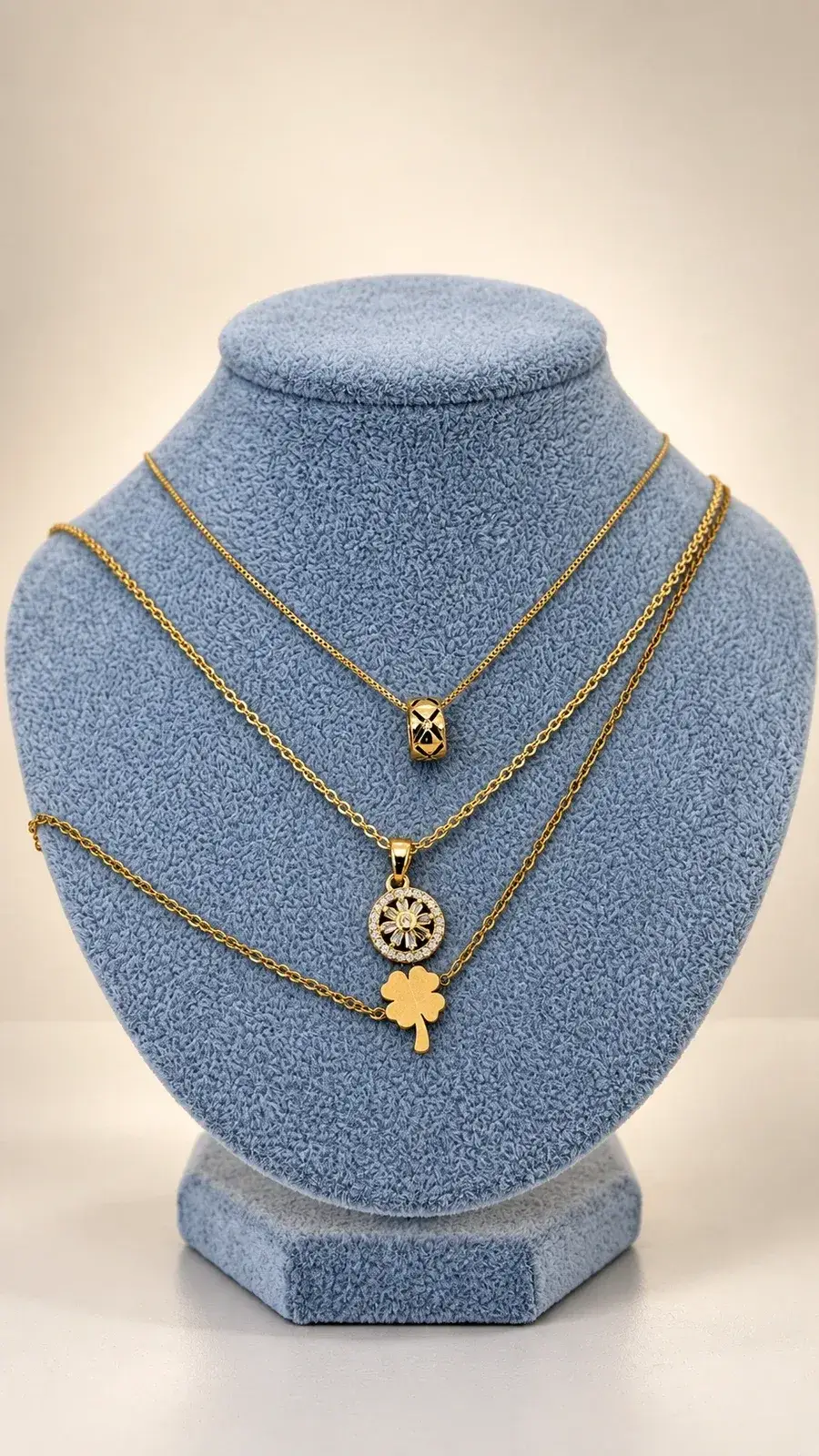 Tres collares dorados con dijes: anillo, medalla con flor y trébol